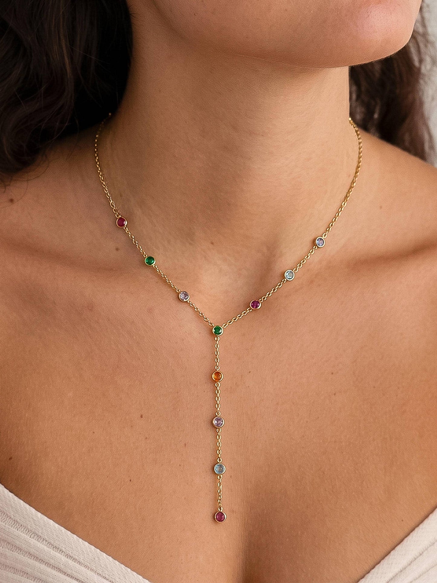 A delicate gold Y-necklace with small multicolored gemstone drops, worn on a model's neck and upper chest.