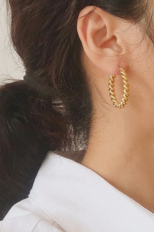 Close-up of a person wearing gold hoop earrings with a neutral background
