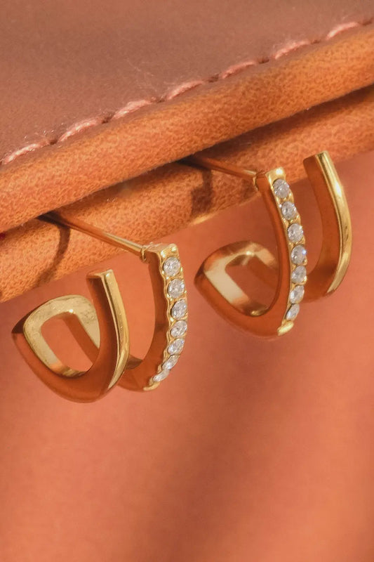 Gold hoop earrings with clear stones on a brown leather surface