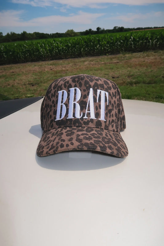 Leopard print cap with 'BRAT' text on a vehicle roof with a cornfield background