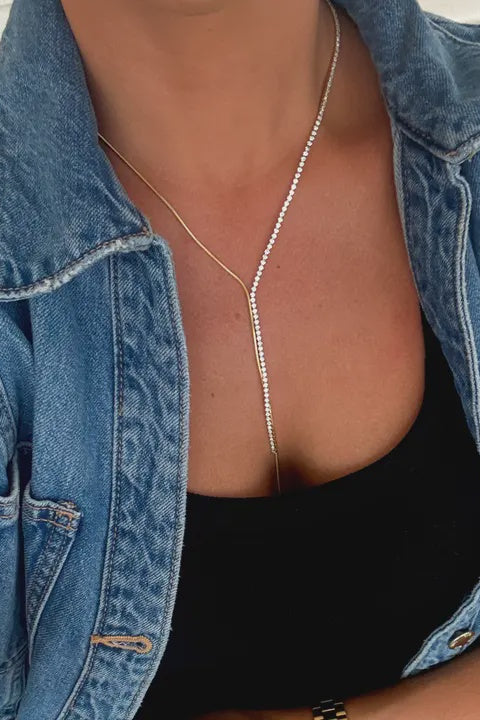 Person wearing a blue denim jacket and black top with a pearl necklace.
