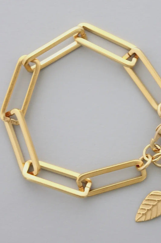 Gold bracelet with geometric design and leaf charm on a gray background