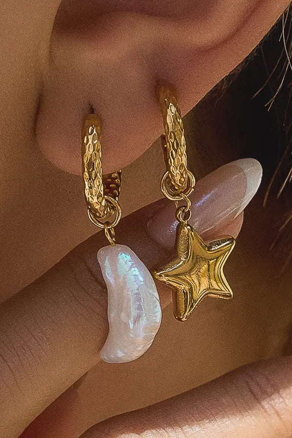 Gold hoop earrings with star and pearl charm worn by a person.