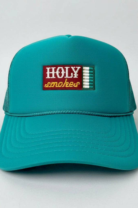 A teal trucker hat with a rectangular embroidered patch on the front that reads 'HOLY smokes' in white and yellow, set against a plain light gray background.