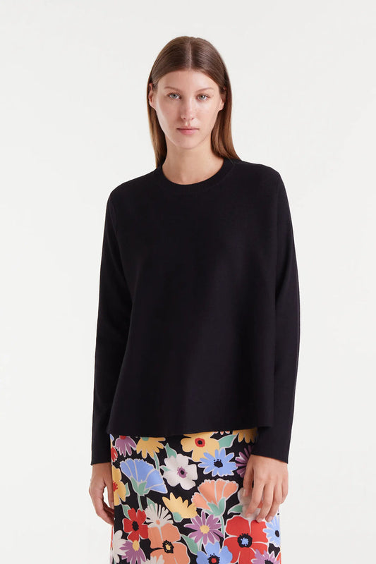 Woman wearing a black sweater over a colorful floral skirt on a white background