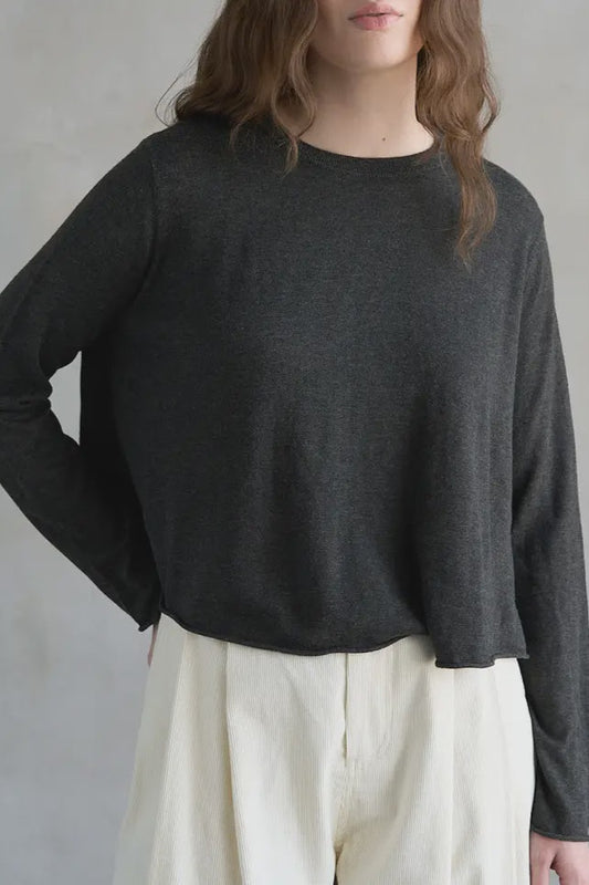 Person wearing a dark gray sweater and light-colored pants against a neutral background