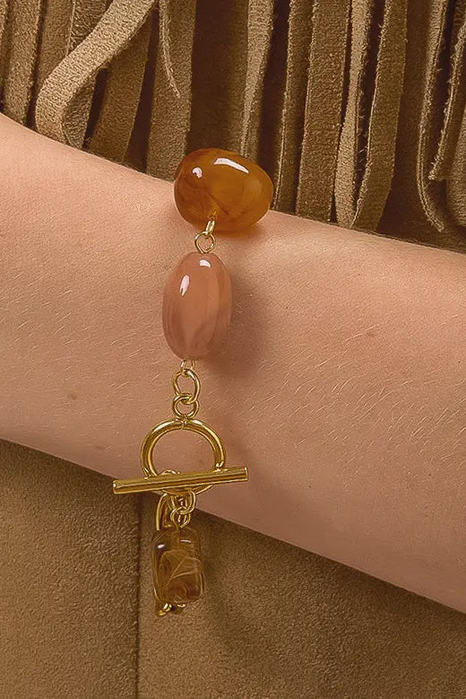 Bracelet with amber beads and gold clasp on a wrist against a brown background