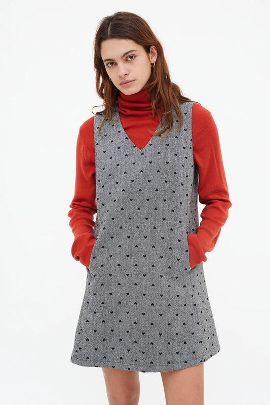 Woman wearing a gray polka dot dress over an orange sweater on a white background