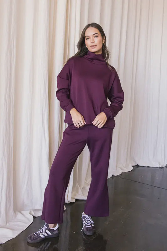 Person wearing a purple tracksuit standing against a white curtain.