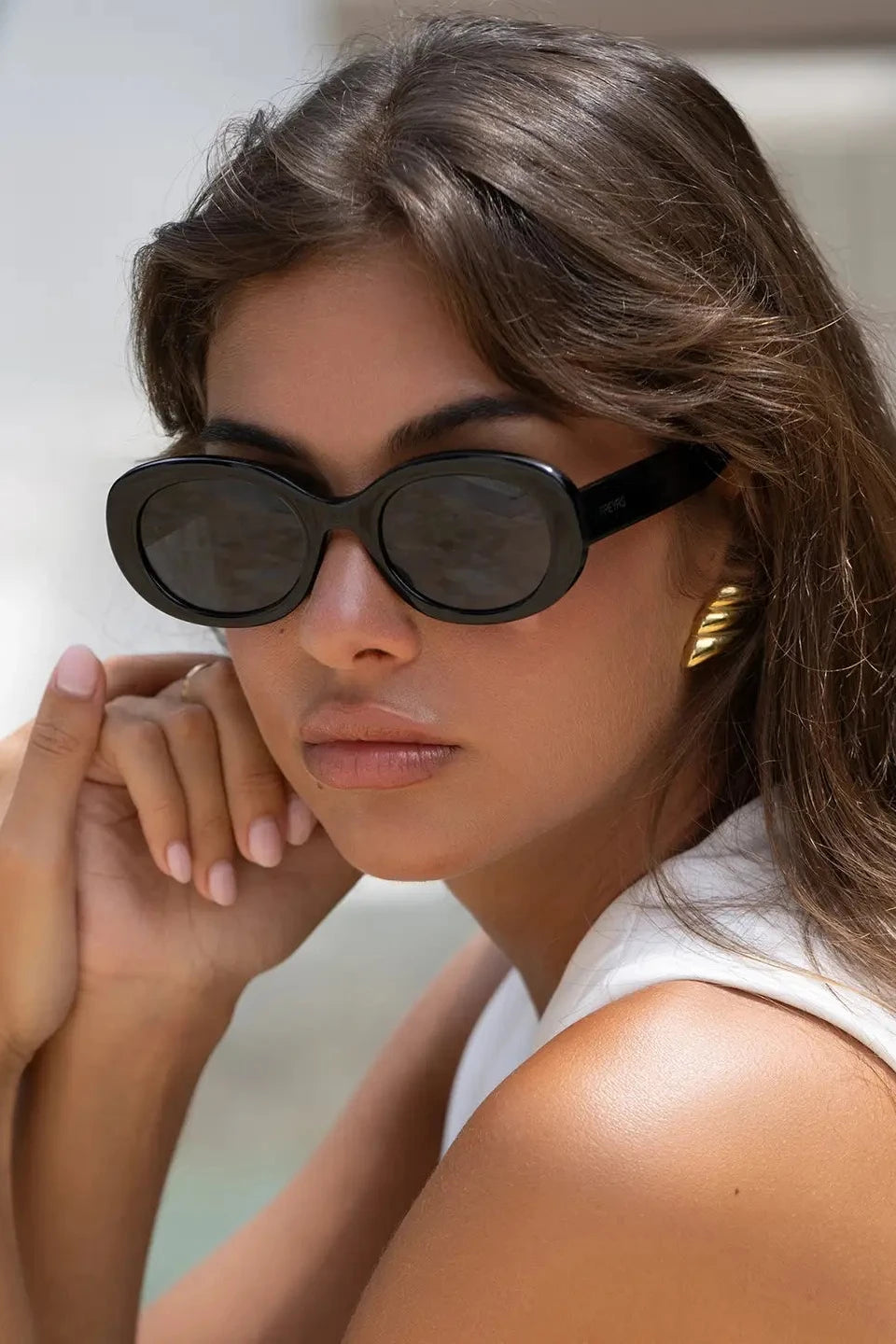 Woman wearing black sunglasses and a white sleeveless top with a blurred background