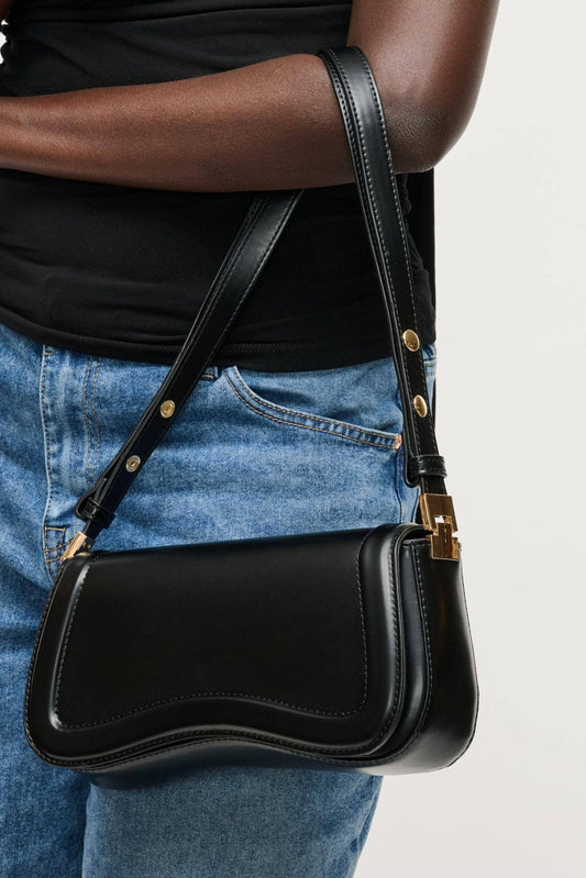 Person wearing a black leather shoulder bag with gold accents on a light gray background