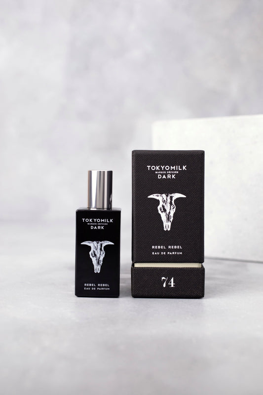 Tokyo Milk Rebel Rebel Dark Eau de Parfum bottle with a silver cap next to its black packaging box, featuring a white bull skull graphic and the number 74, set on a light gray marble surface.