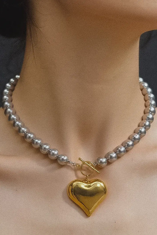 Pearl necklace with a gold heart pendant on a person against a dark background