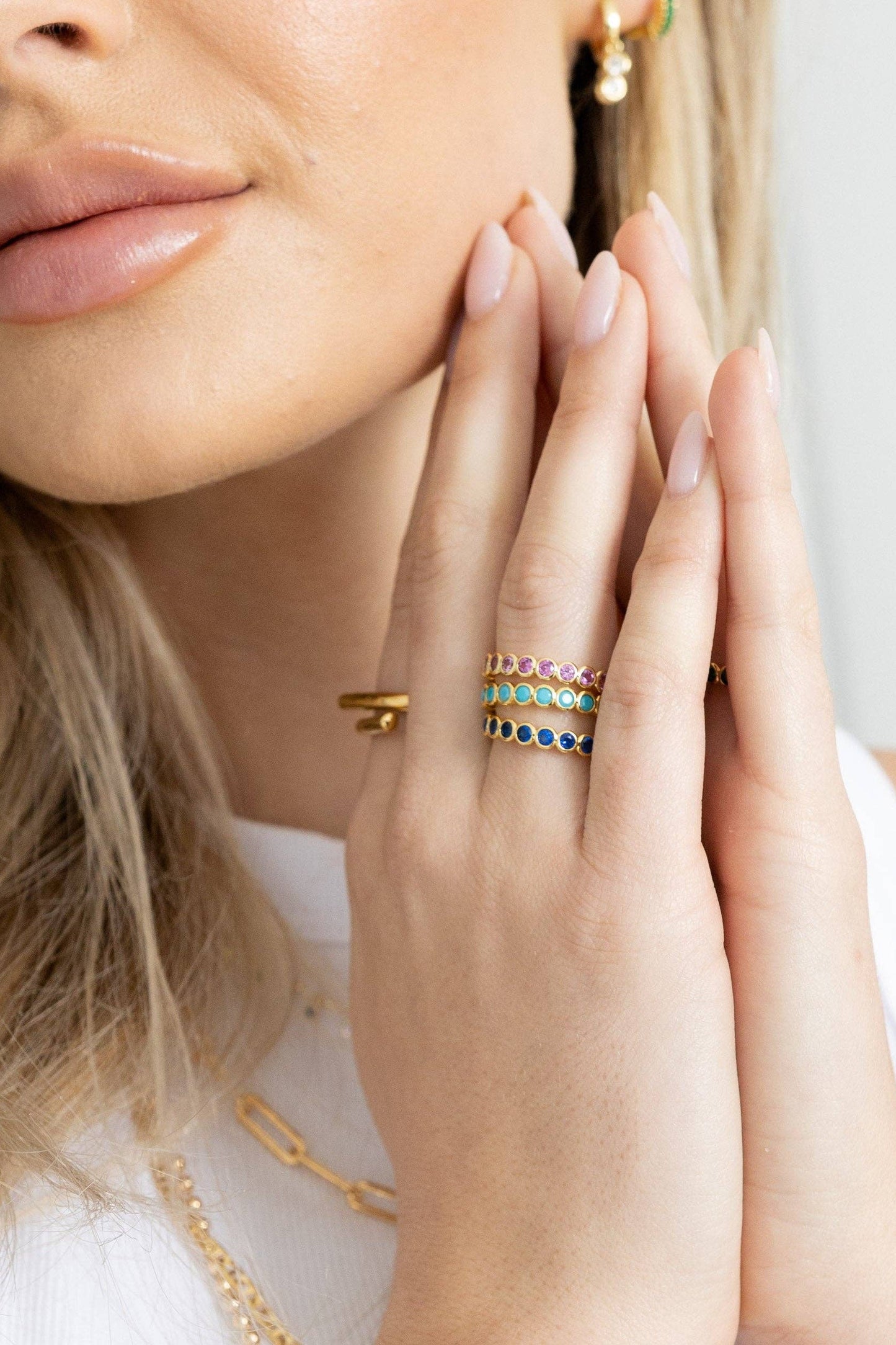 Close-up of a woman's face with gold jewelry on her fingers and neck.