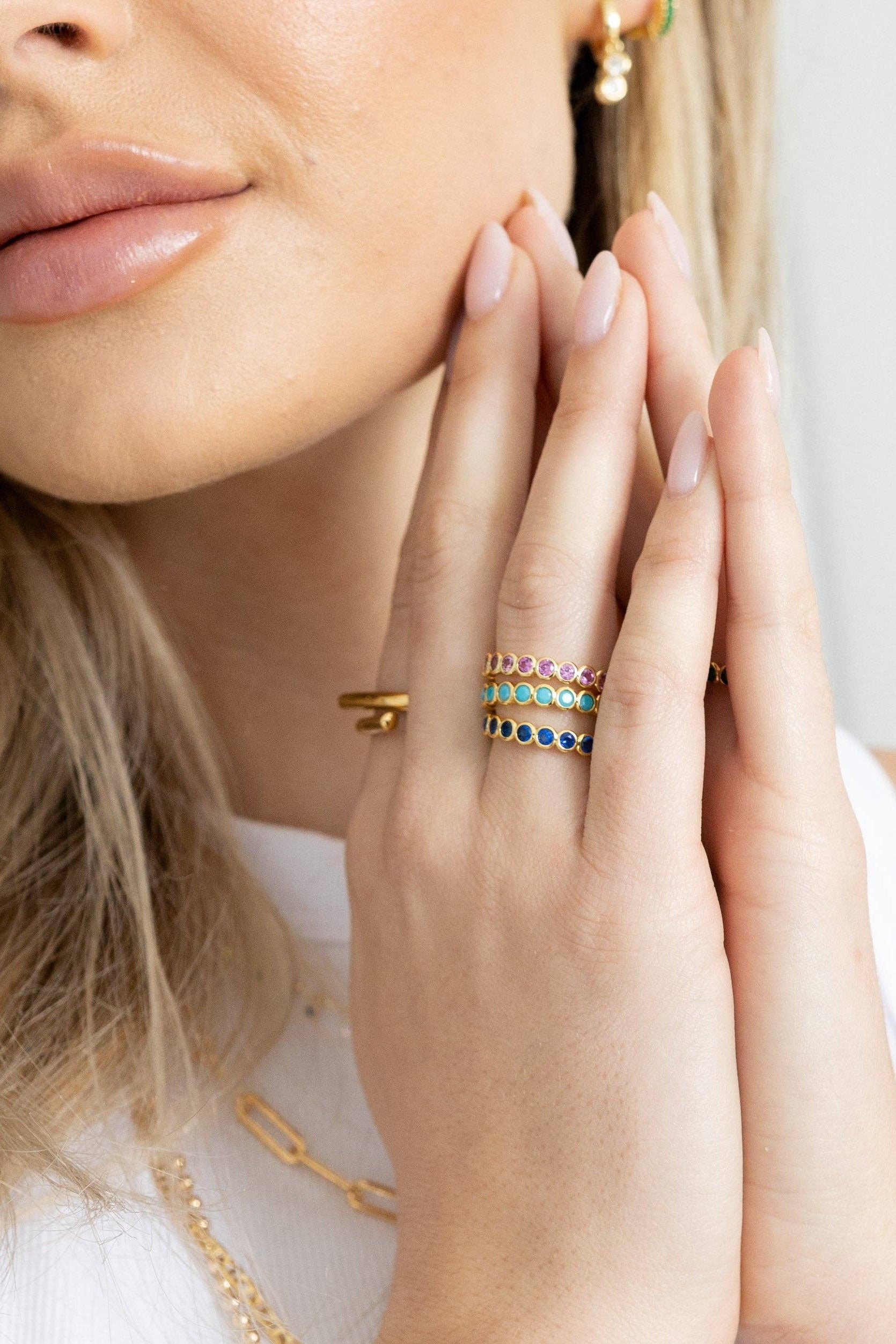 Close-up of a woman's face with gold jewelry on her fingers and neck.