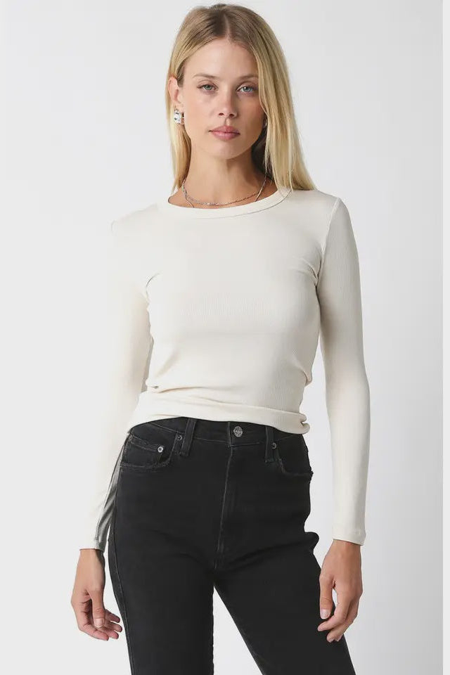 Woman wearing a white long-sleeve top and black jeans against a white background