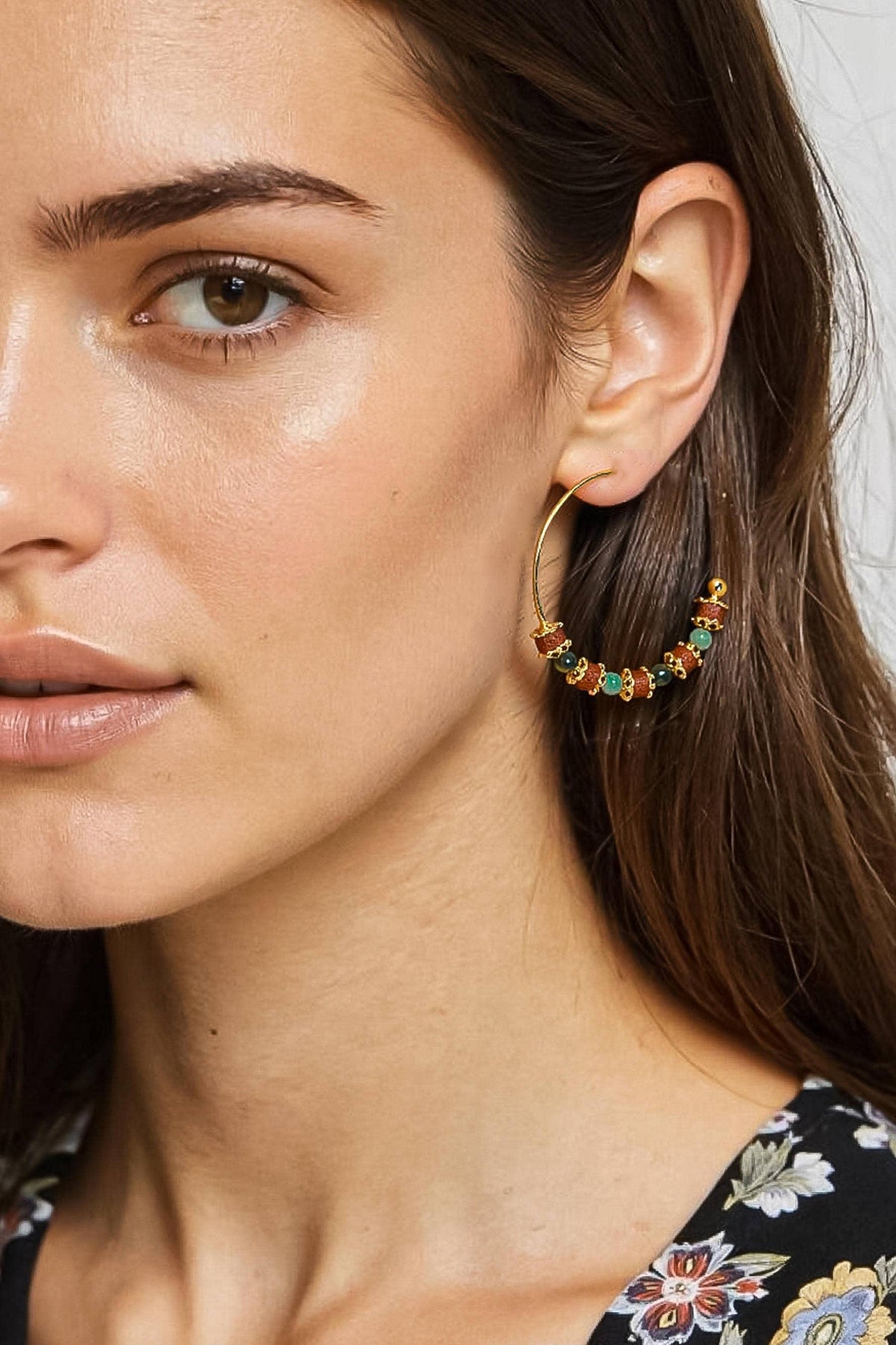 A close-up of a woman wearing a large gold hoop earring adorned with small colorful gemstones, including green, orange, and red.