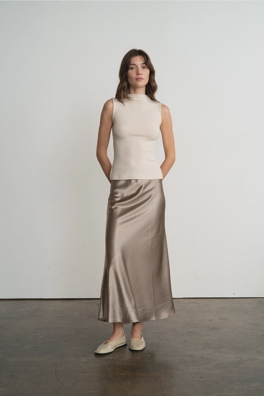 Woman wearing a beige sleeveless top and satin skirt against a white background