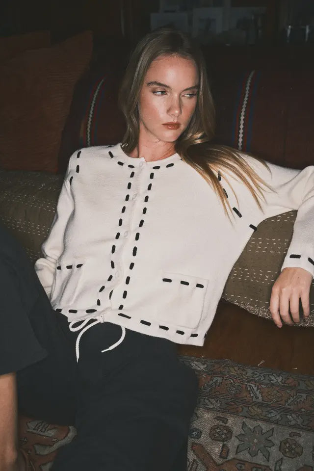 Woman wearing a white cardigan with black accents sitting on a patterned rug.