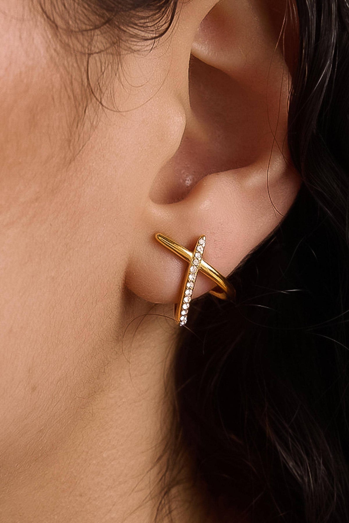 A close-up of a person's ear wearing a gold C-shaped ear cuff with a small row of clear stones along one arm of the C.