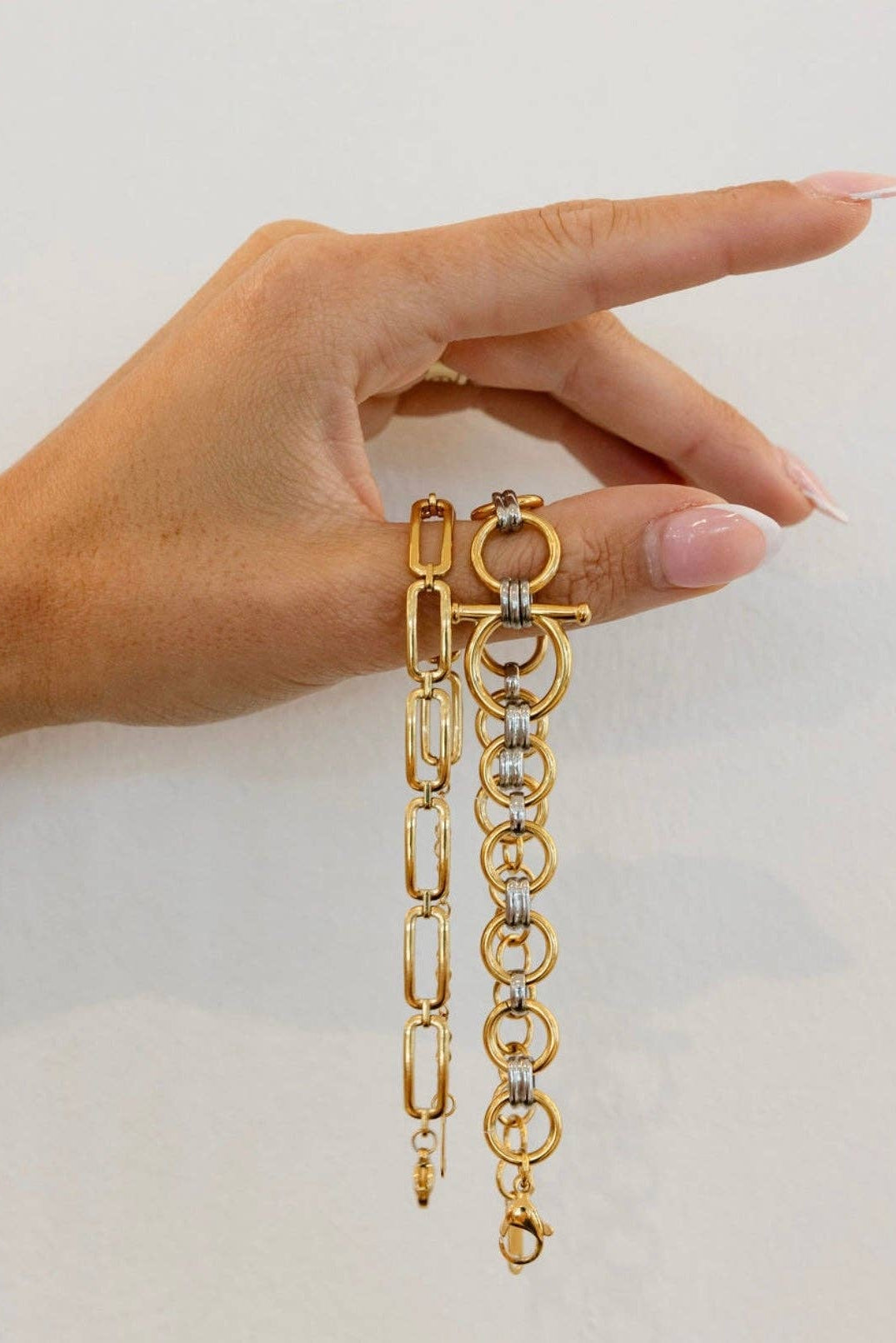Gold chain bracelet held by a hand against a plain background