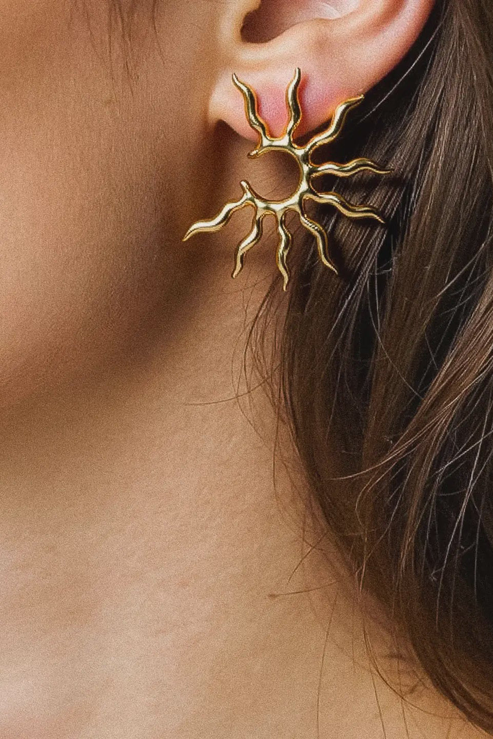 Gold sun-shaped earring worn by a person with brown hair.