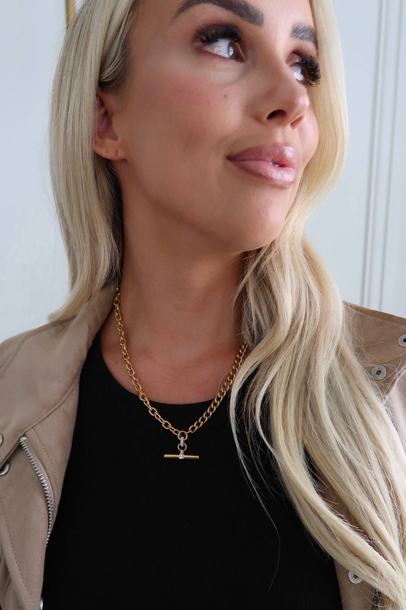 Woman wearing a gold necklace with a pendant, looking to the side.