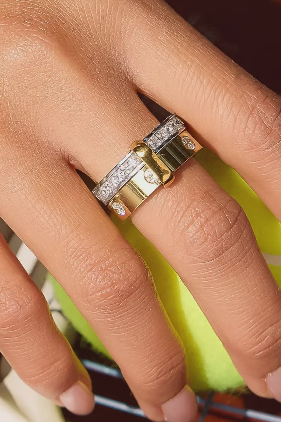 Close-up of a hand wearing a gold ring with diamond accents on a blurred background