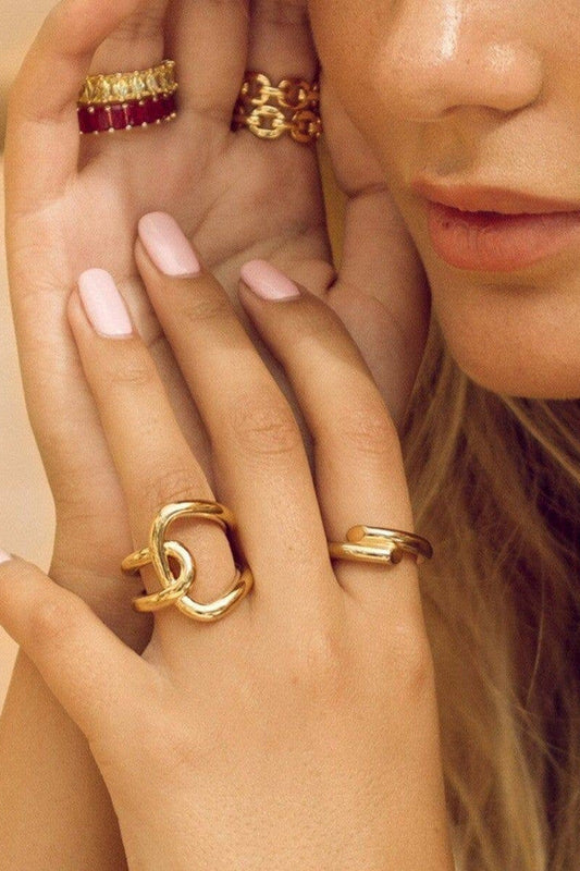 Close-up of a hand wearing multiple gold rings with a neutral background