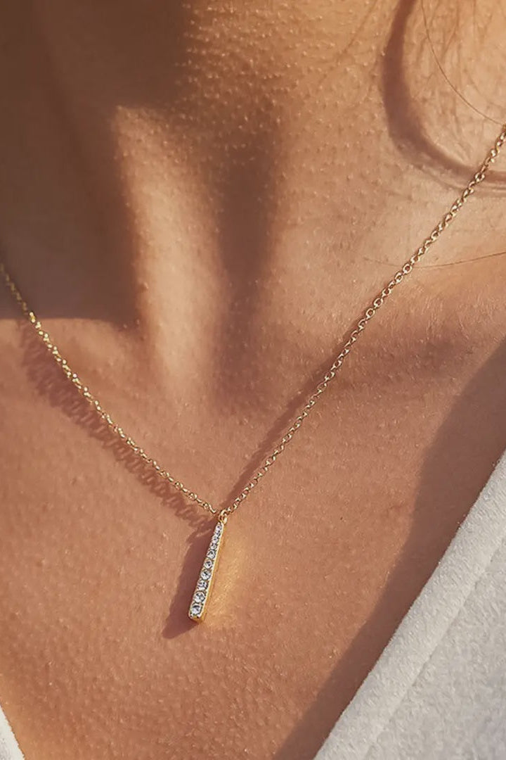 Gold necklace with a small diamond pendant on a person wearing a light-colored top.