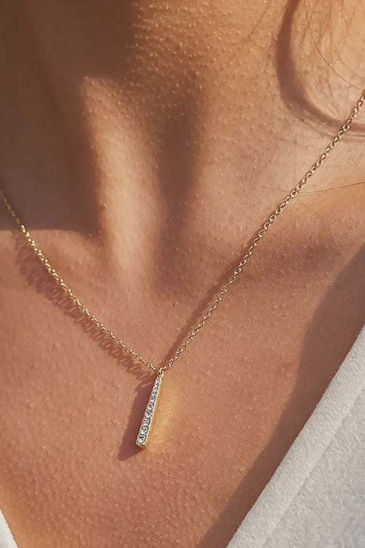 Gold necklace with a small diamond pendant on a person wearing a light-colored top.