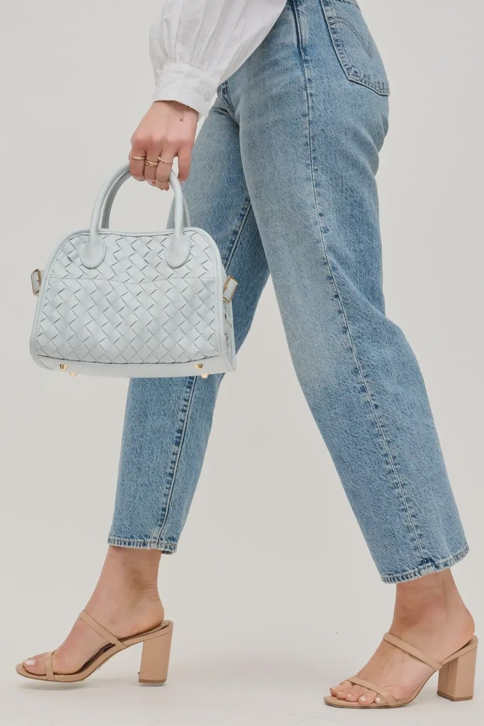 Person holding a light blue woven handbag with a plain background