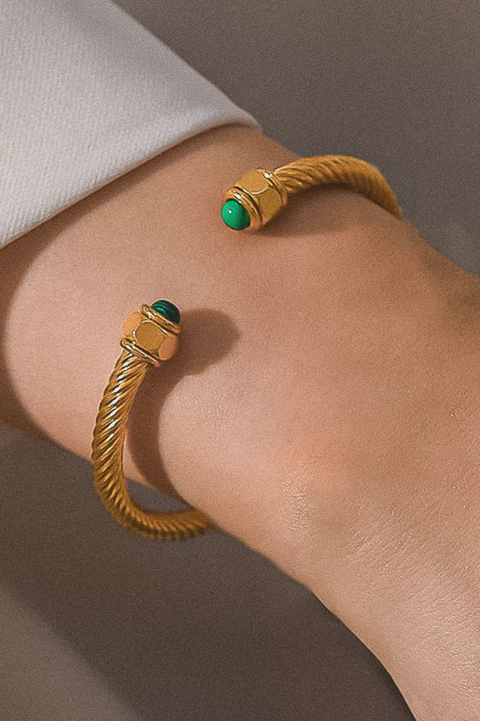 Gold bracelet with green gemstones on a wrist against a neutral background
