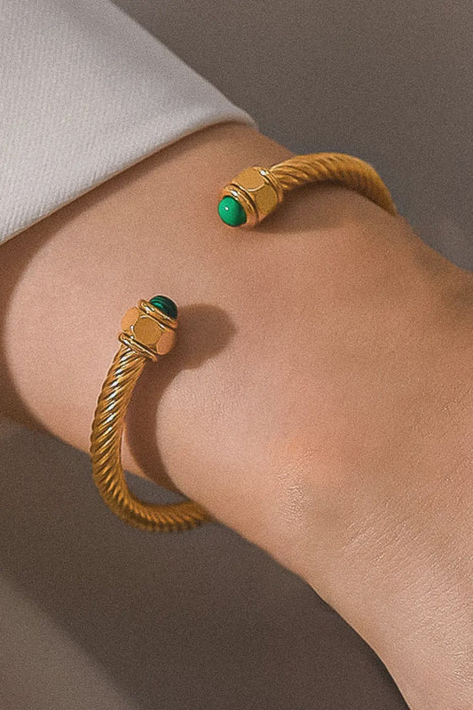 Gold bracelet with green gemstones on a wrist against a neutral background