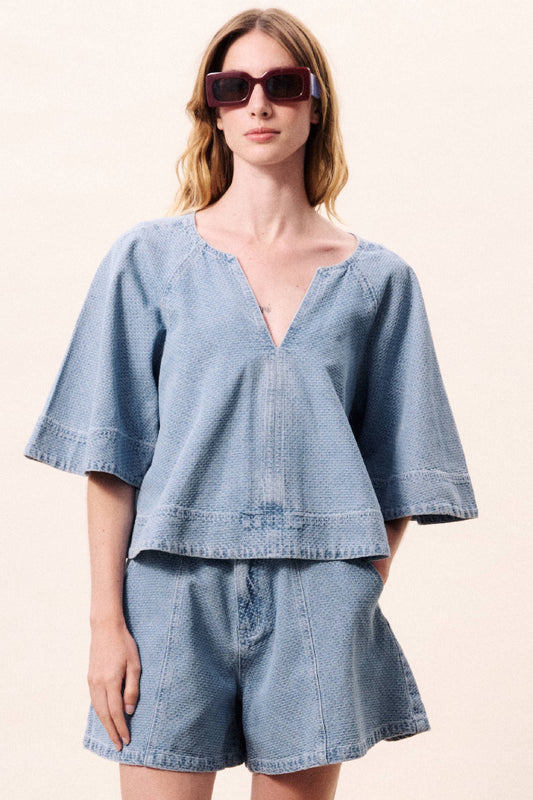 Woman wearing a denim outfit with sunglasses on a plain background