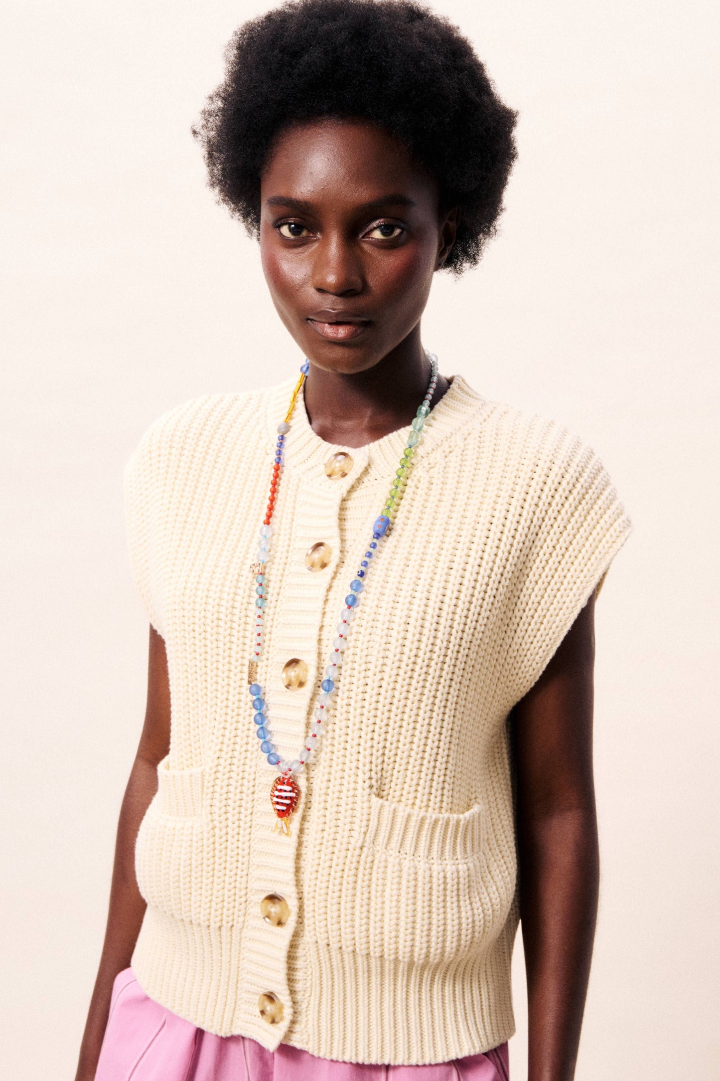 Woman wearing a beige knitted vest with a plain background