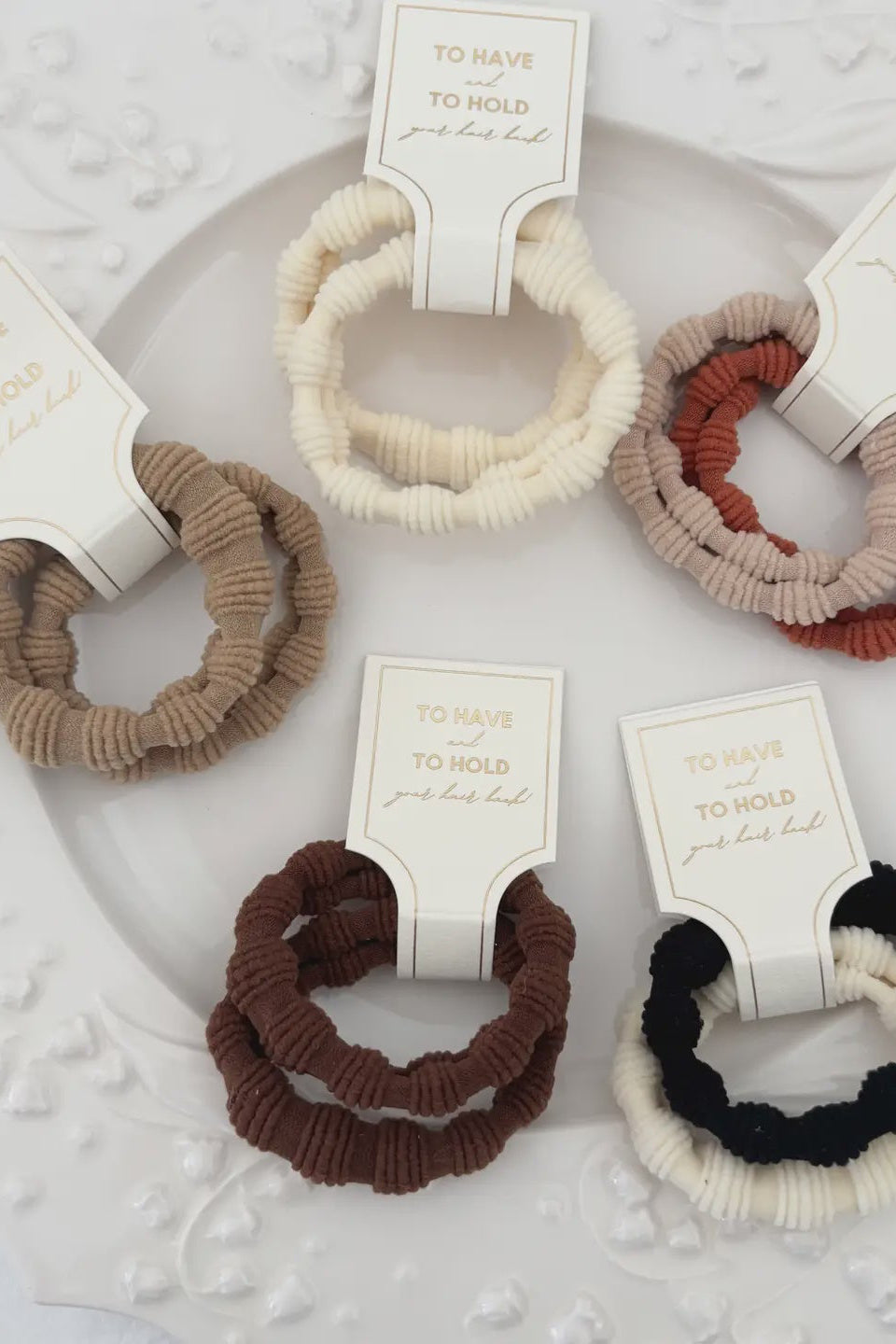 Set of five hair scrunchies in different colors with tags on a textured white surface
