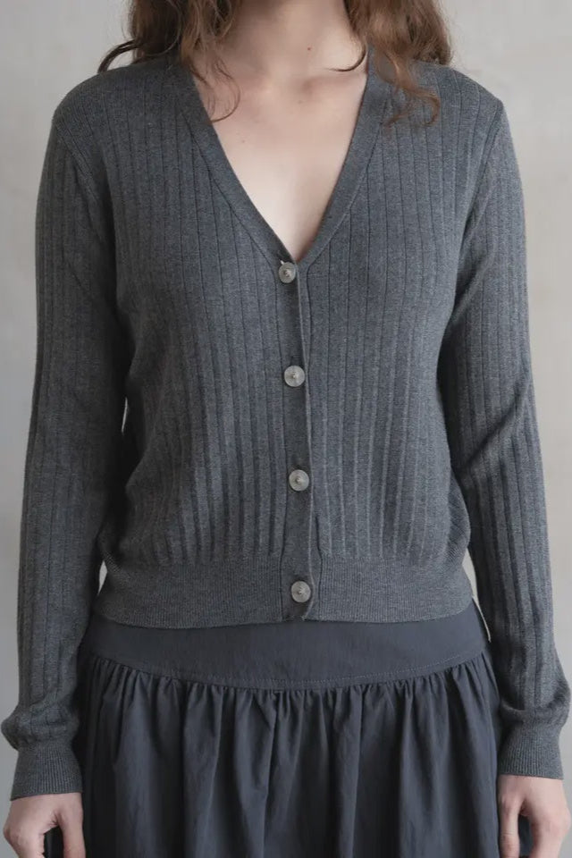 Person wearing a gray ribbed sweater with buttons on a plain background