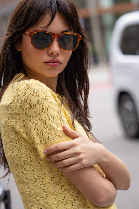 Woman wearing sunglasses and a yellow top on a city street
