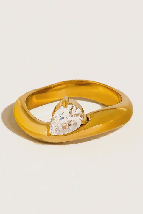 Gold ring with a heart-shaped diamond on a light beige background