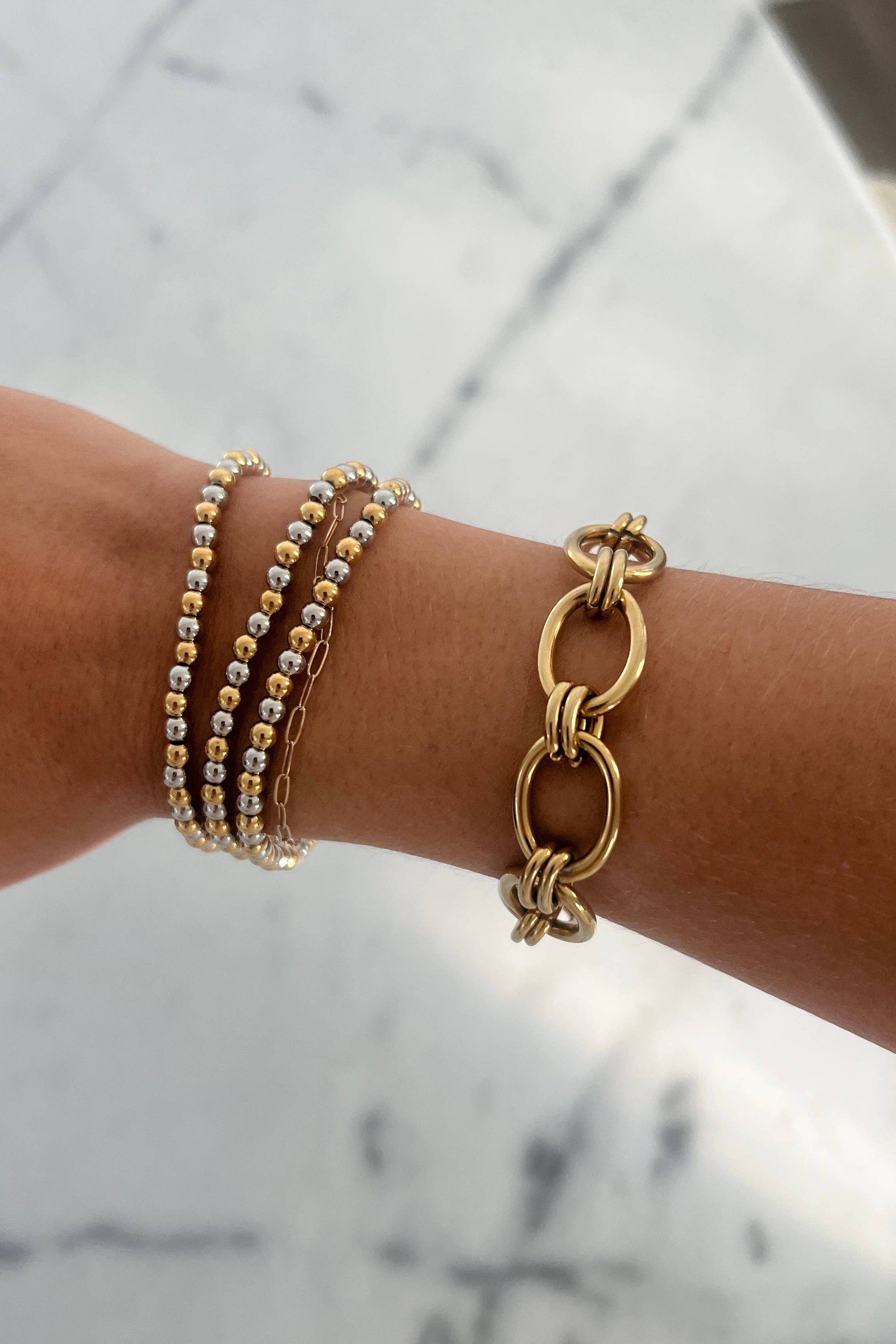 Gold bracelets on a wrist with a marble background