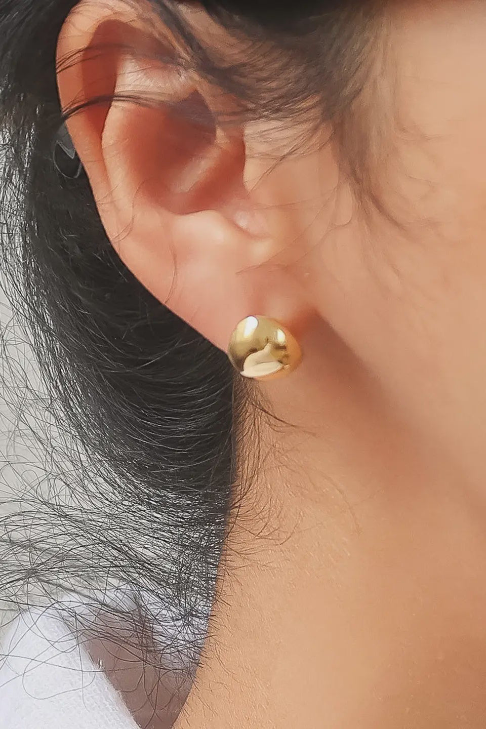 Close-up of an ear wearing a gold earring with blurred background