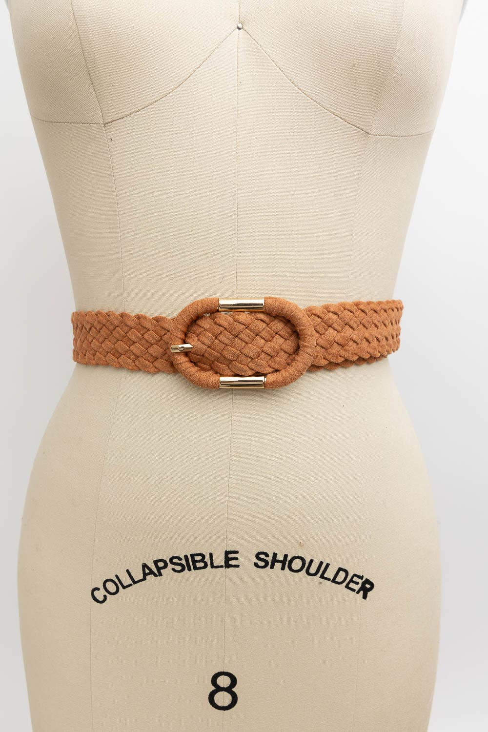 A tan braided belt with a large oval buckle, displayed on a beige dress form mannequin against a white background.