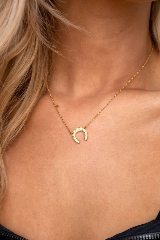 Gold necklace with a horseshoe pendant on a person's neck