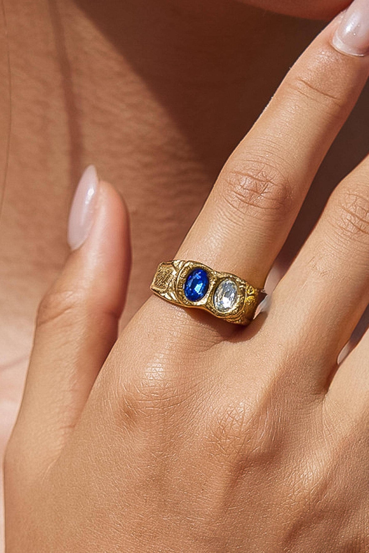 A gold ring with a central oval blue gemstone and a smaller round clear gemstone, worn on a person's finger.