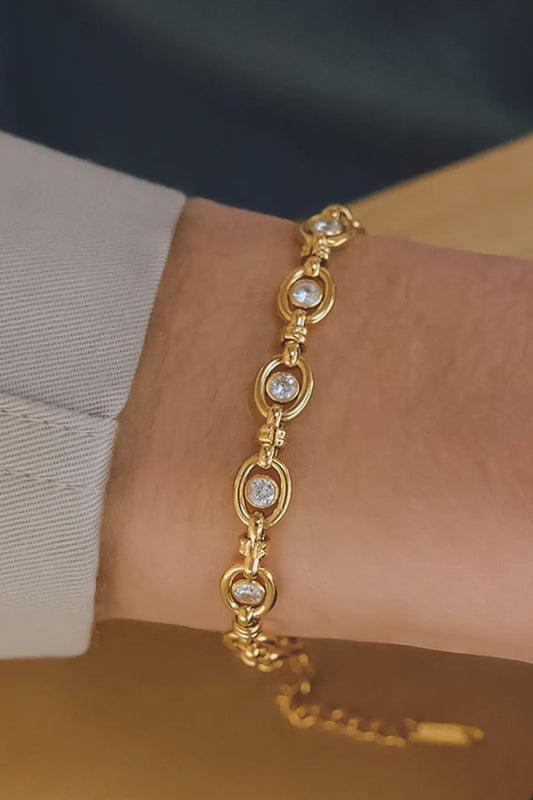 Gold bracelet with heart-shaped links worn on a wrist against a neutral background