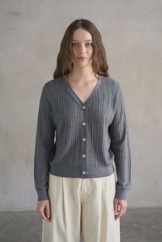 Woman wearing a gray knitted cardigan against a plain background