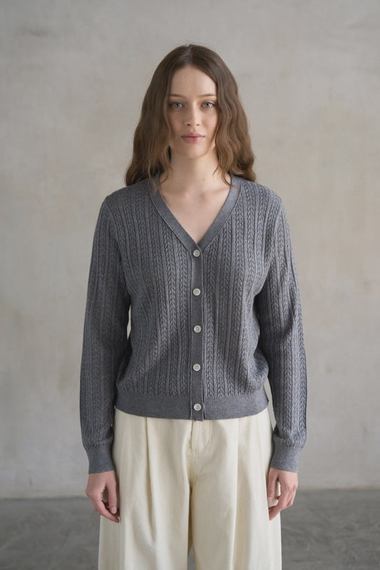 Woman wearing a gray knitted cardigan against a plain background