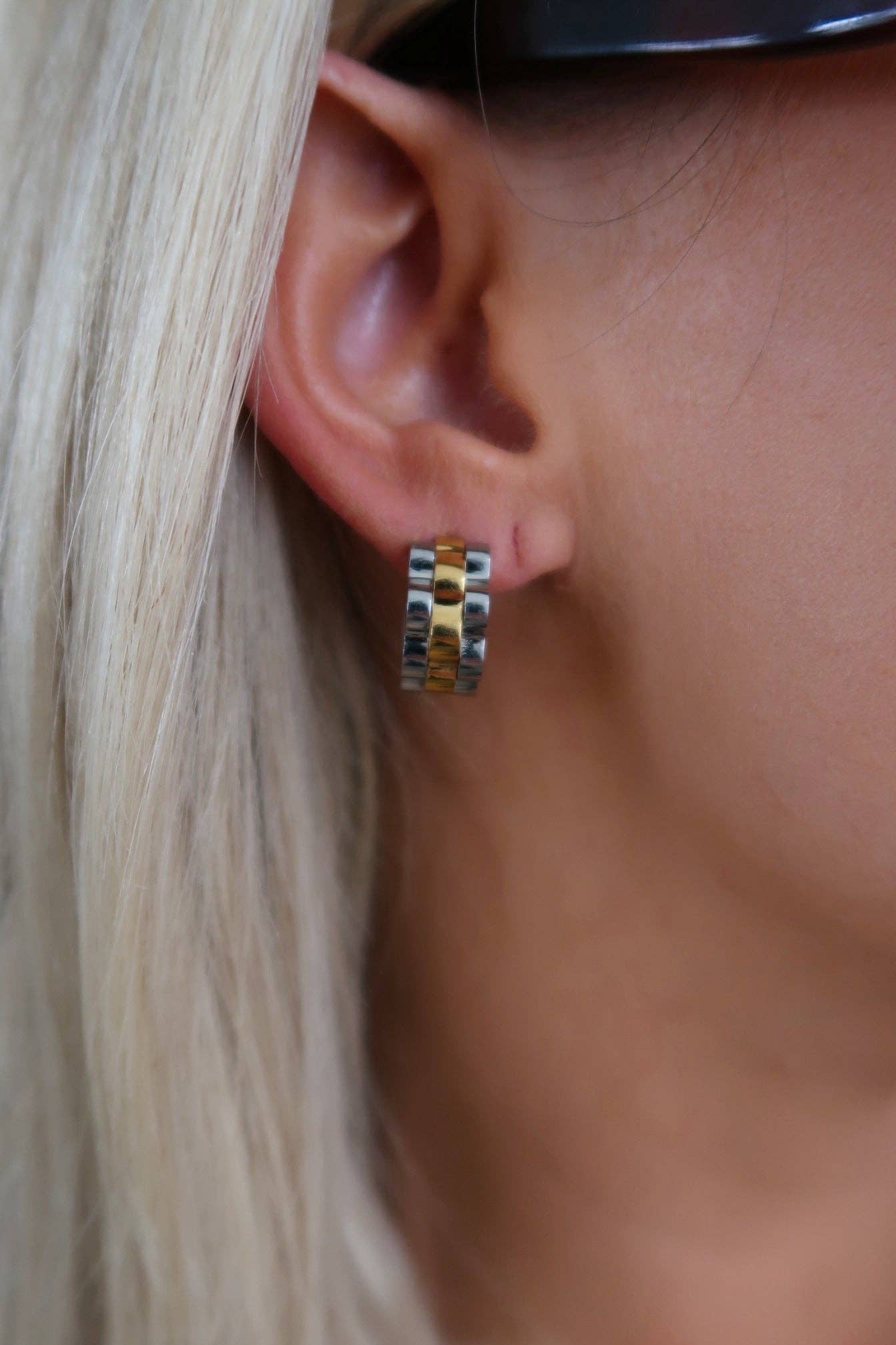 Close-up of an ear wearing a small hoop earring with blonde hair partially visible.