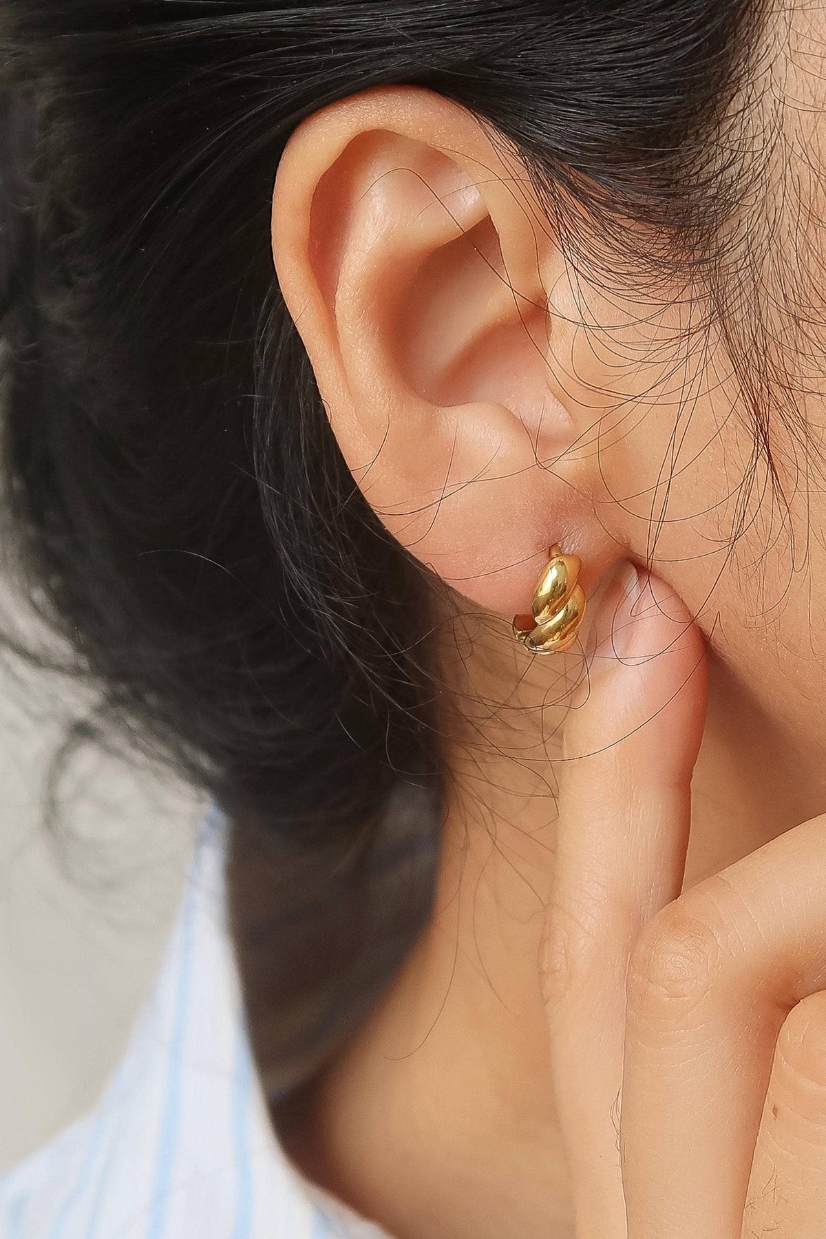 Close-up of a person wearing a gold earring with a blurred background